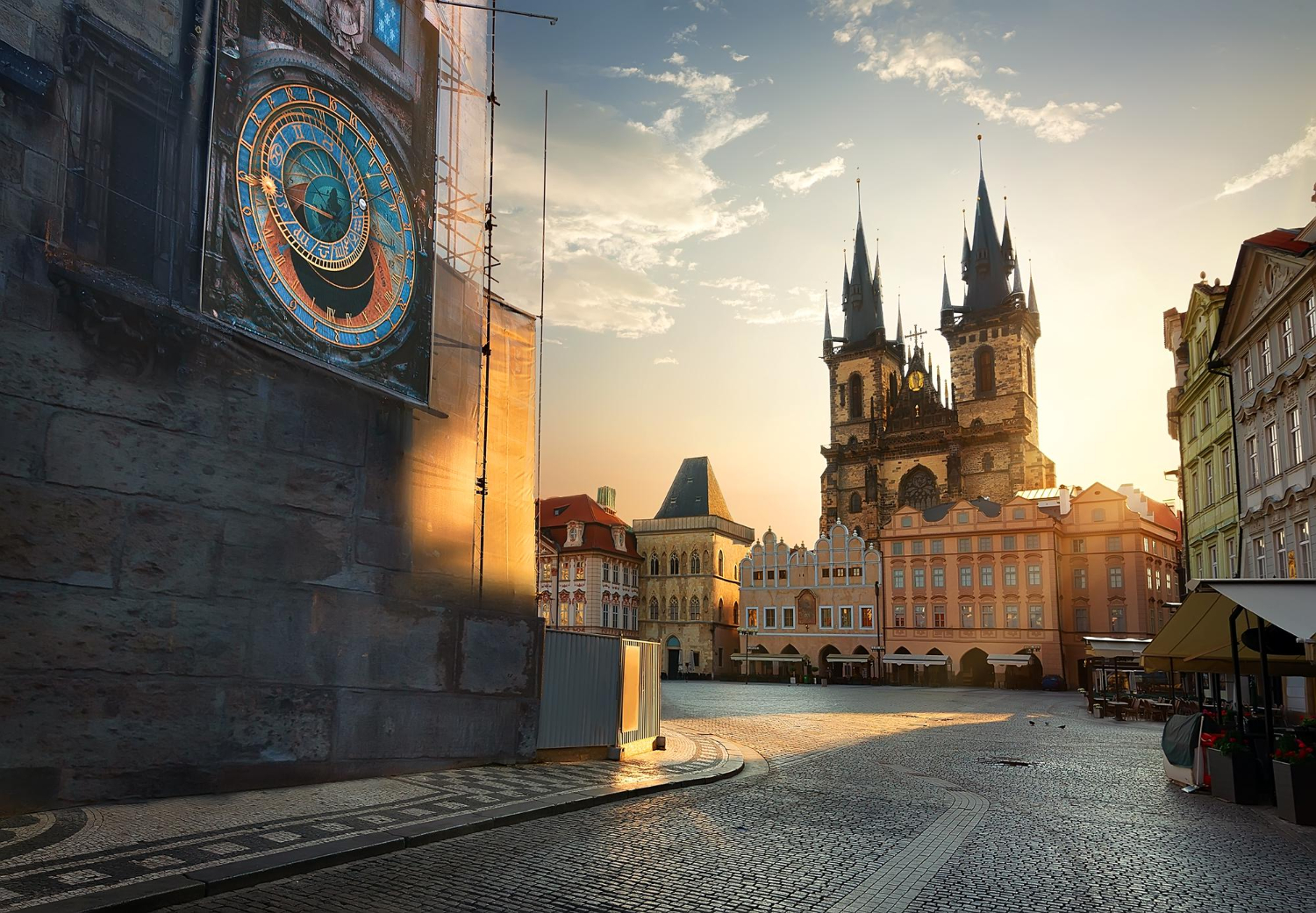 Sunlit Prague square with the historic Astronomical Clock on the left and the Gothic Church of Our Lady before Týn in the background.